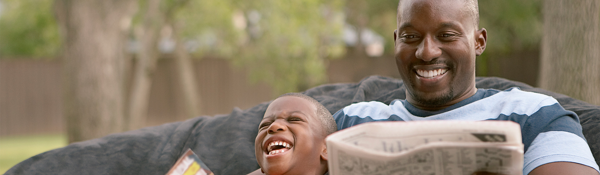 Father and son laugh while reading outside