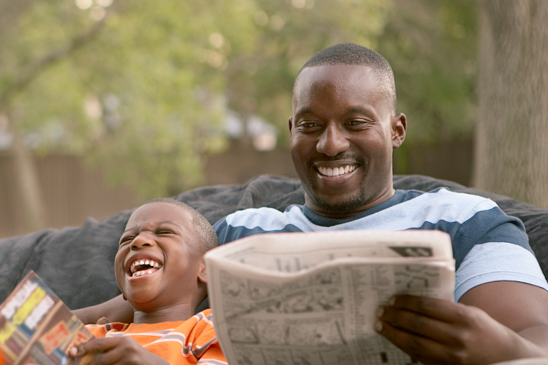 Father and son laugh while reading outside